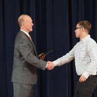 Doctor Potteiger shaking hands with an award recipient in a white patterned shirt
